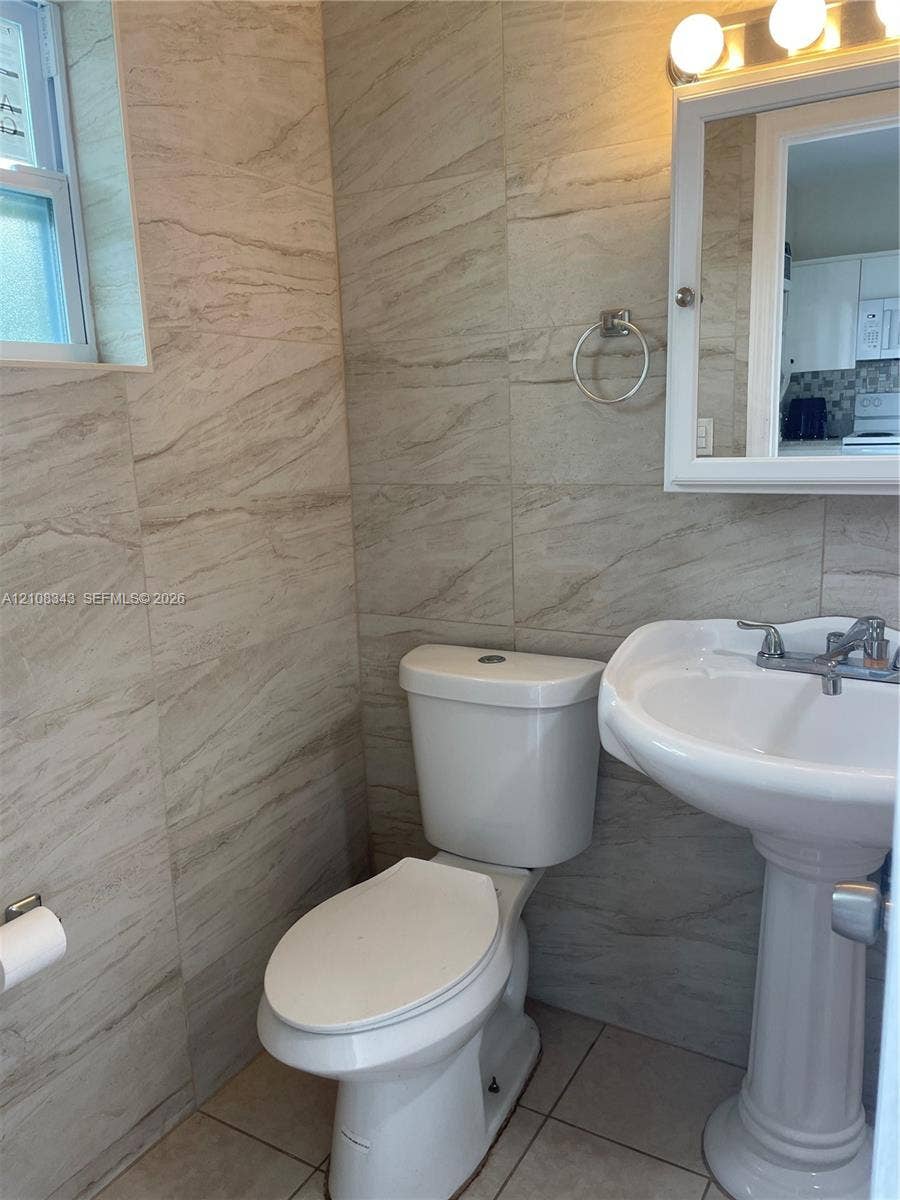 1935 Liberty Street, #3, Hollywood, Hollywood, FL 33020 Full-height stone-finish wall tile, white pedestal sink, polished chrome faucet, wall-mounted medicine cabinet, and three-bulb vanity lighting