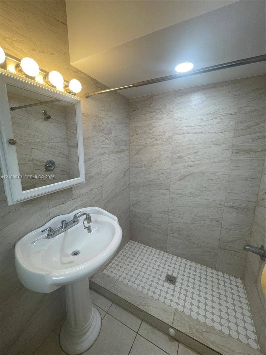 1935 Liberty Street, #3, Hollywood, Hollywood, FL 33020 Bathroom featuring floor-to-ceiling neutral stone-finish tile, walk-in shower with penny-round floor tile, pedestal sink with chrome faucet, and mirrored medicine cabinet with integrated four-light fixture