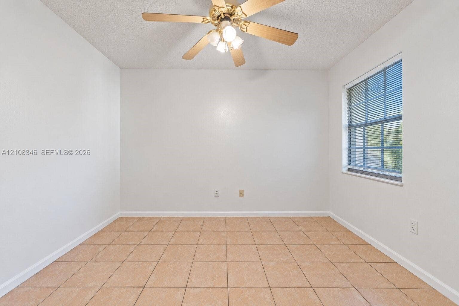 2530 SE 7th Place, Homestead, FL 33033 Neutral-toned square tile flooring, light-filled interior with single-pane window, and ceiling-mounted fan with integrated light fixture