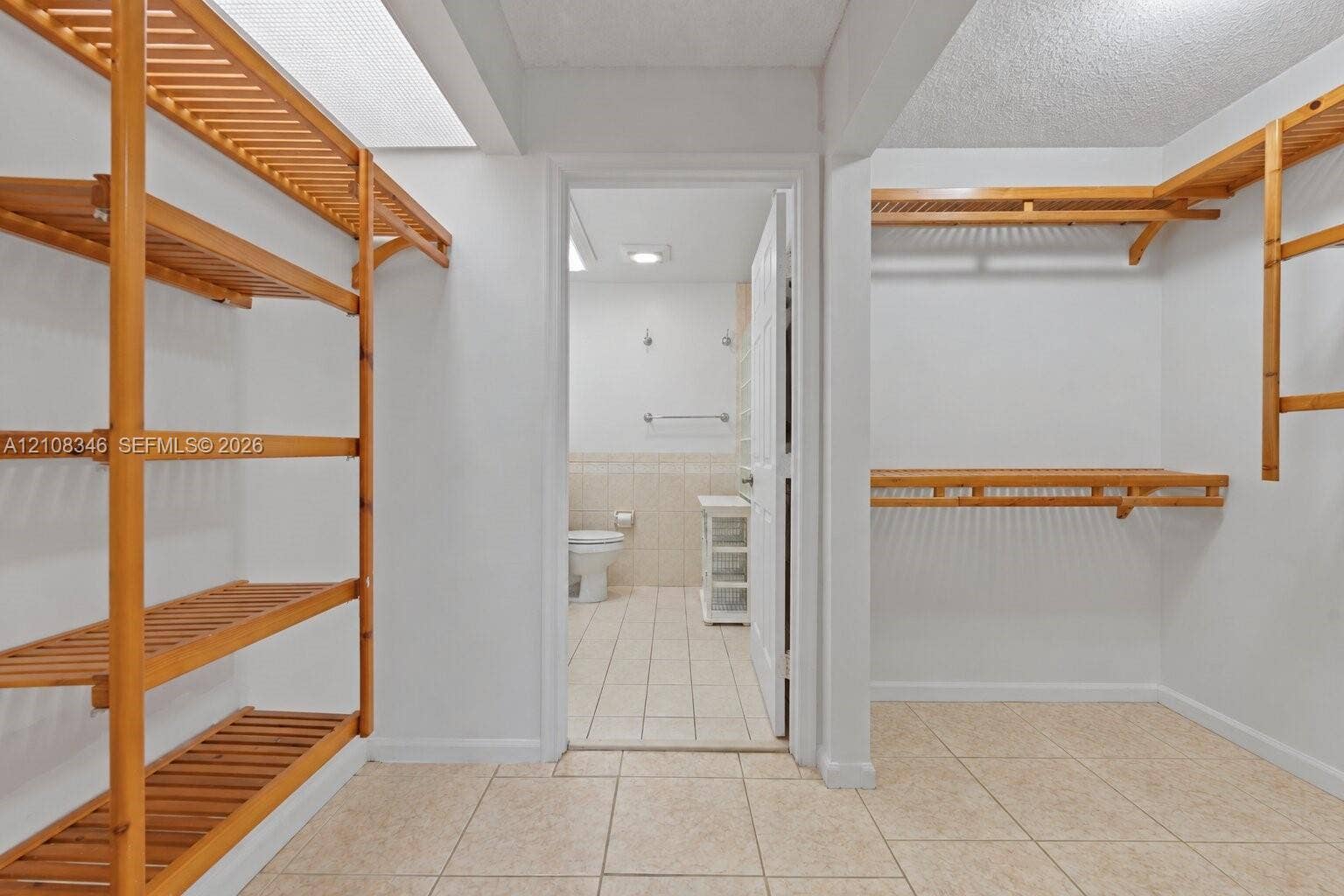 2530 SE 7th Place, Homestead, FL 33033 Walk-in closet featuring light-toned tile flooring and custom wood slatted shelving, with entry to a bathroom showcasing tile wainscoting and a white vanity cabinet