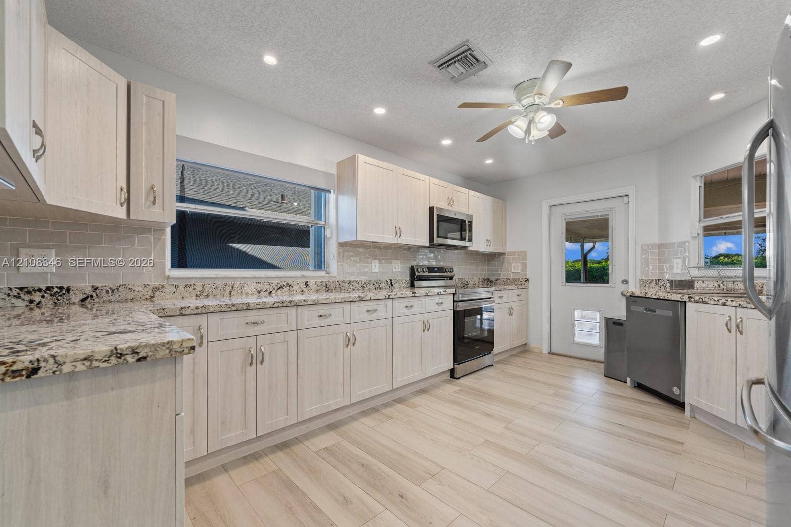 2530 SE 7th Place, Homestead, FL 33033 Kitchen featuring light-toned cabinetry, stone countertops, subway tile backsplash, stainless steel appliances, and wood-tile flooring