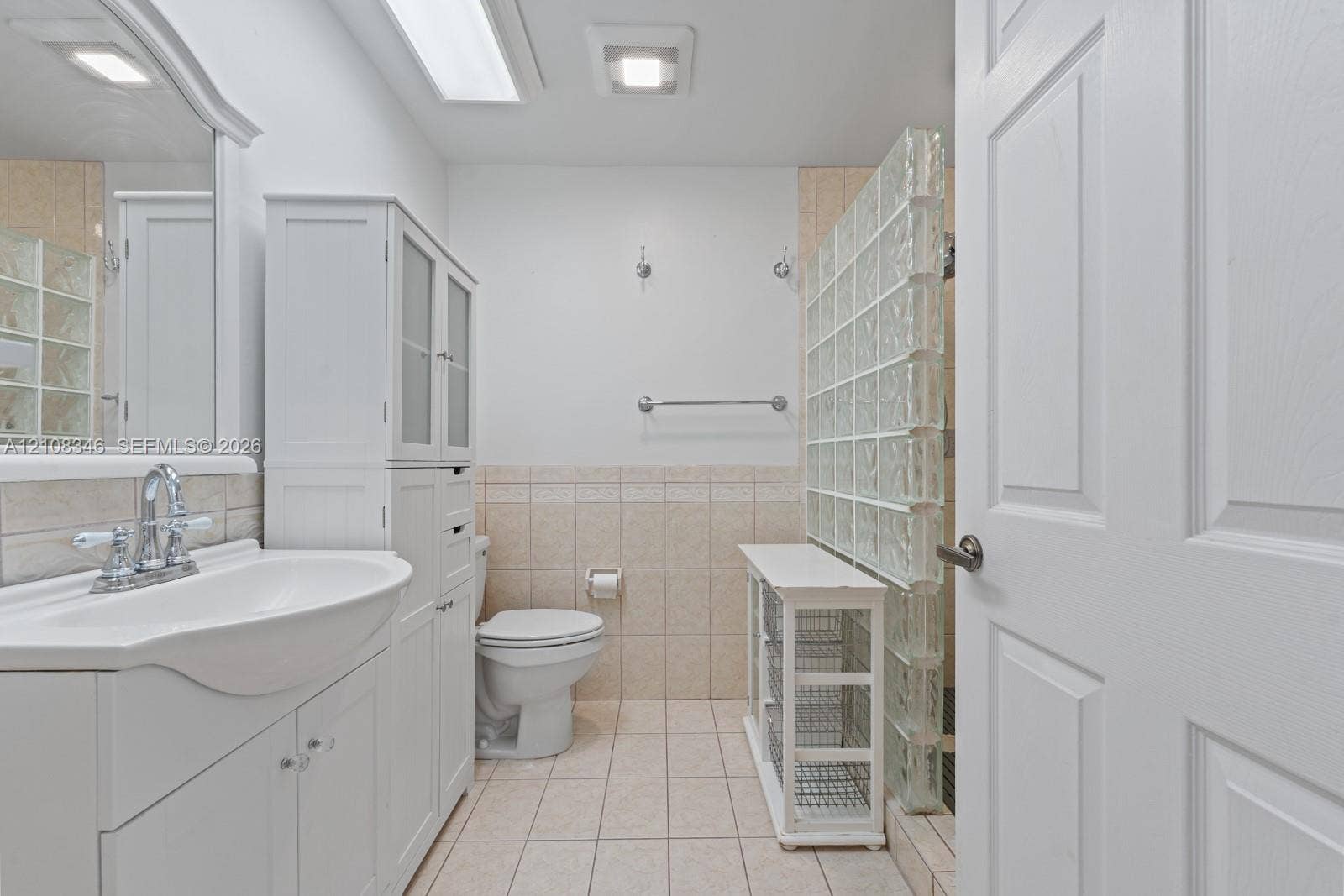 2530 SE 7th Place, Homestead, FL 33033 Bathroom featuring a white vanity cabinet with an integrated sink, ceramic tile flooring, neutral wall-to-wall ceramic tiling, and a glass block privacy partition
