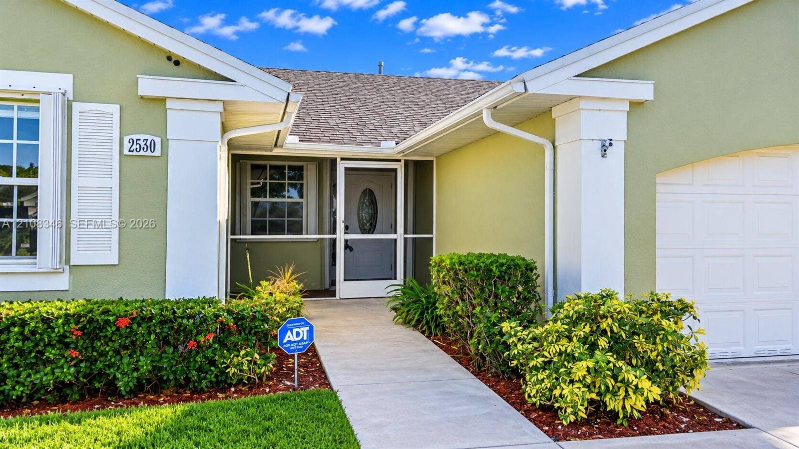 2530 SE 7th Place, Homestead, FL 33033 Stucco exterior featuring decorative shutters, a covered entryway with a screened storm door, a concrete walkway, and an attached garage