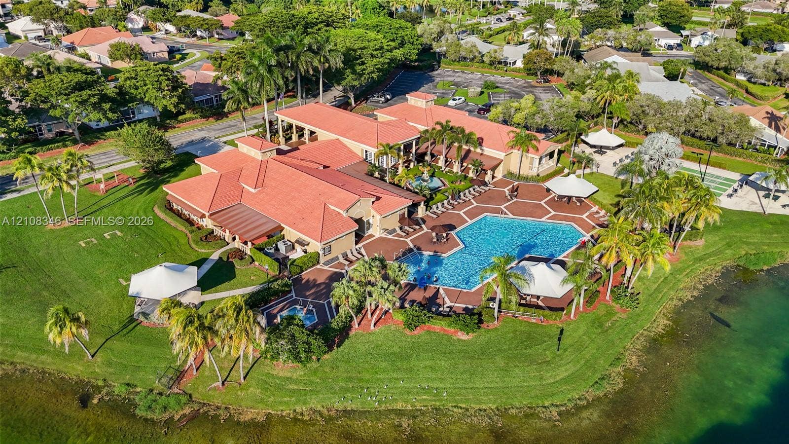 2530 SE 7th Place, Homestead, FL 33033 Aerial view of a clubhouse in the community center featuring a tile-roofed structure, a large swimming pool, an attached spa, paved patio decking, and landscaped grounds