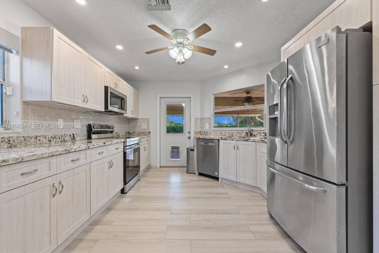 2530 SE 7th Place, Homestead, FL 33033 Kitchen featuring light-toned cabinetry, stone-finish countertops, stainless steel appliances, tile backsplash, and wood-tile flooring and exterior door to lani