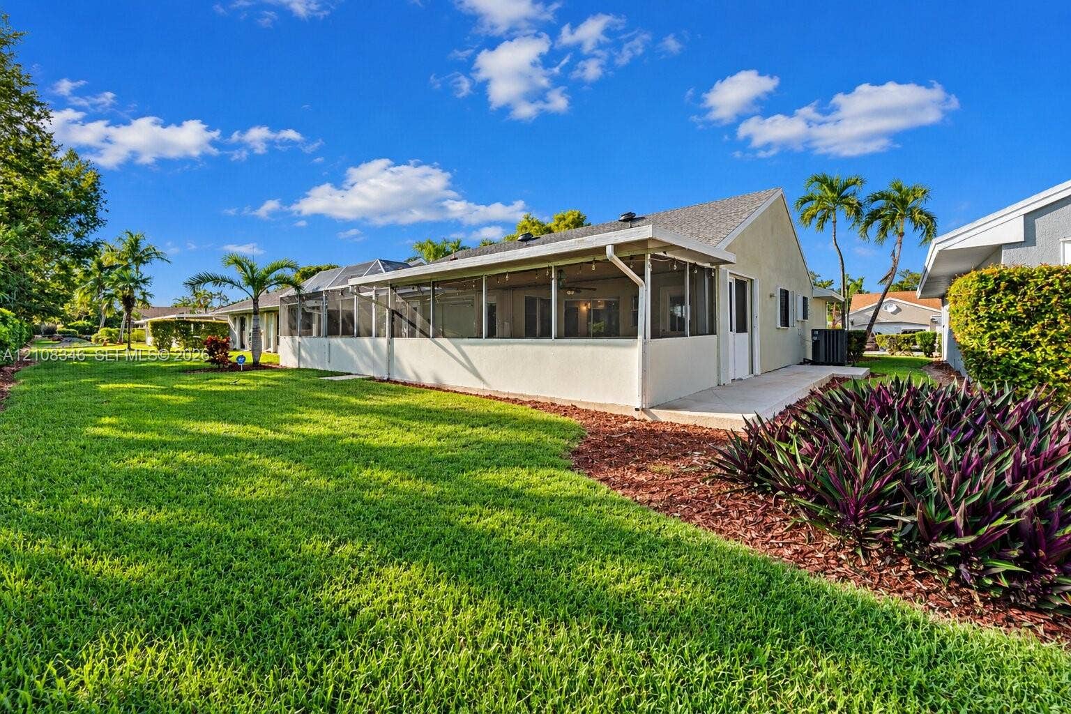 2530 SE 7th Place, Homestead, FL 33033 Exterior rear elevation featuring a screened-in lanai, concrete patio, expansive lawn, mature palm trees, and mulched landscaping beds