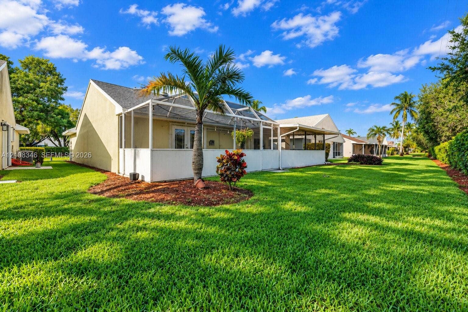 2530 SE 7th Place, Homestead, FL 33033 Rear exterior featuring a screened-in lanai, manicured lawn, palm trees, and ground-level plantings