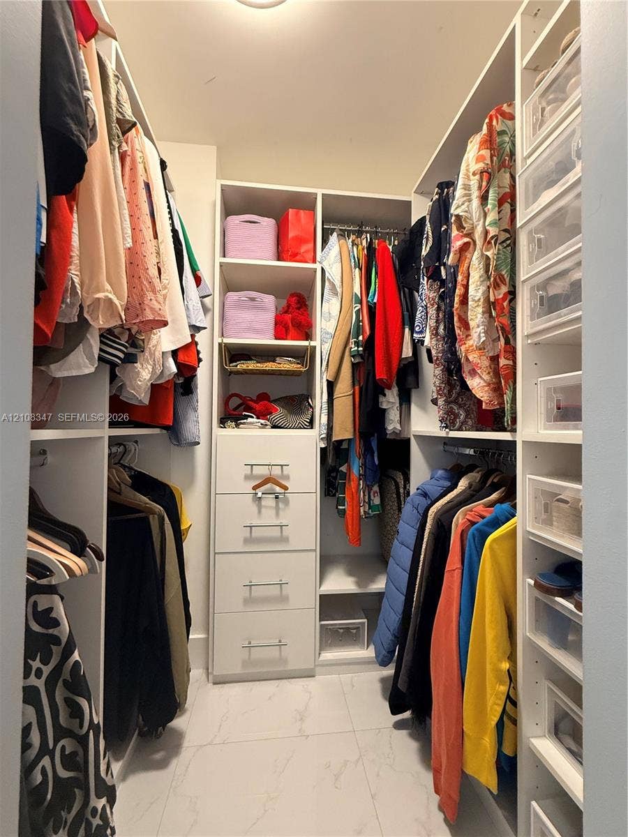 Walk-in closet featuring white built-in shelving, integrated dresser drawers with bar-pull hardware, hanging rods, and large-format tile flooring
