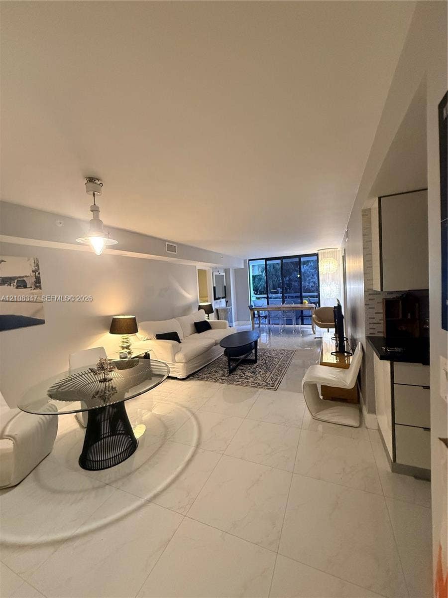 Open-concept floor plan featuring large-format polished tile flooring, recessed ceiling lighting, a contemporary pendant light fixture, and floor-to-ceiling glass sliding doors