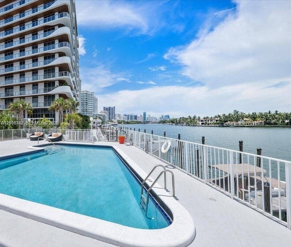 Waterfront swimming pool with concrete decking, perimeter metal fencing, and a private dock