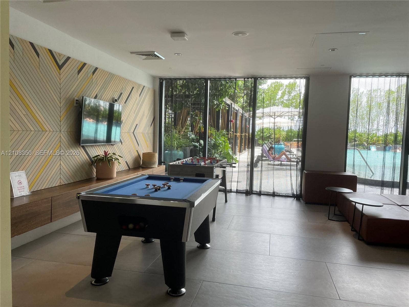 121 NE 34th Street, #1403, Miami, Miami, FL 33137 Recreation room featuring large-format porcelain tile flooring, geometric accent wall paneling, built-in floating wood cabinetry, and floor-to-ceiling glass panel windows