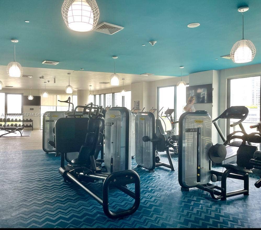 121 NE 34th Street, #1403, Miami, Miami, FL 33137 Fitness center featuring floor-to-ceiling windows, blue chevron-patterned flooring, suspended globe pendant lighting, and multiple wall-mounted televisions