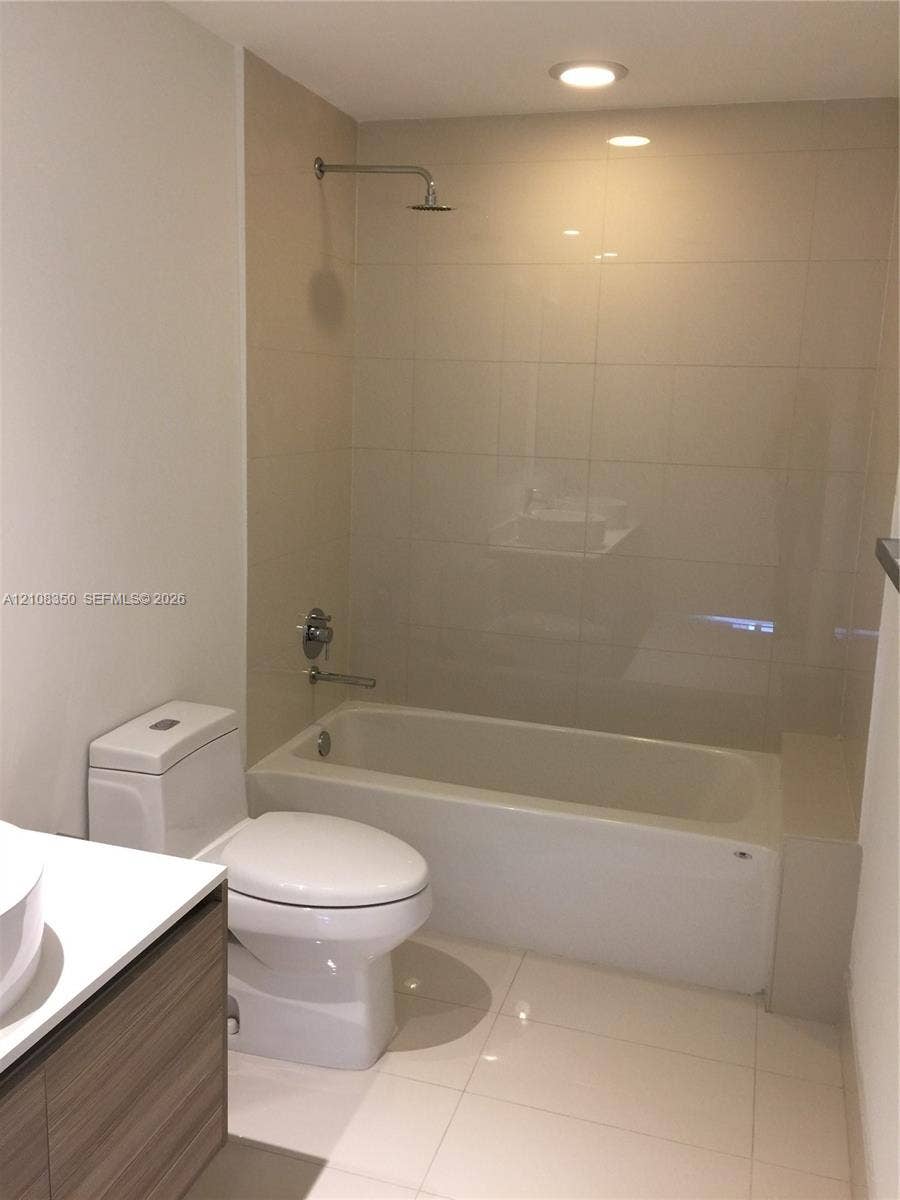 121 NE 34th Street, #1403, Miami, Miami, FL 33137 Full-height neutral wall tiling, bathtub with integrated shower, vanity with wood-finish cabinetry, white countertop, and recessed ceiling lighting