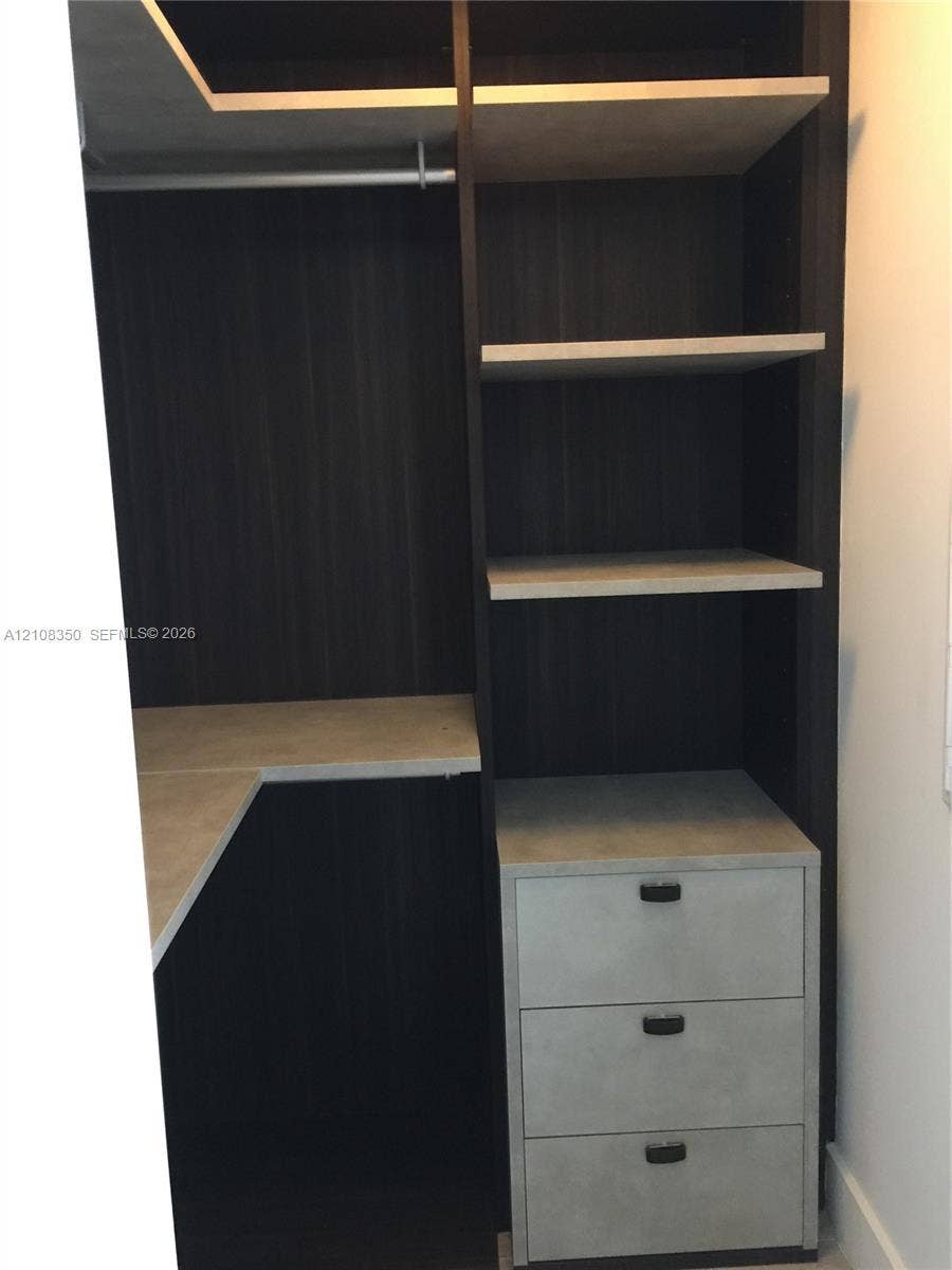 121 NE 34th Street, #1403, Miami, Miami, FL 33137 Custom built-in storage featuring a dark wood-finish frame, light-toned shelving, three integrated drawers with matte hardware, and a metal garment rod