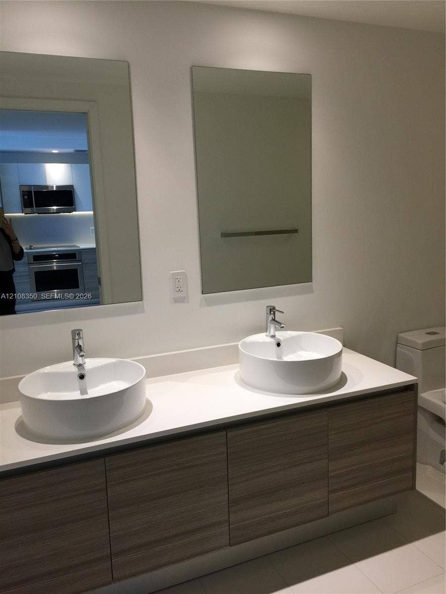 121 NE 34th Street, #1403, Miami, Miami, FL 33137 Floating vanity with wood-finish cabinetry, white countertop, dual vessel sinks, chrome faucets, and rectangular wall mirrors