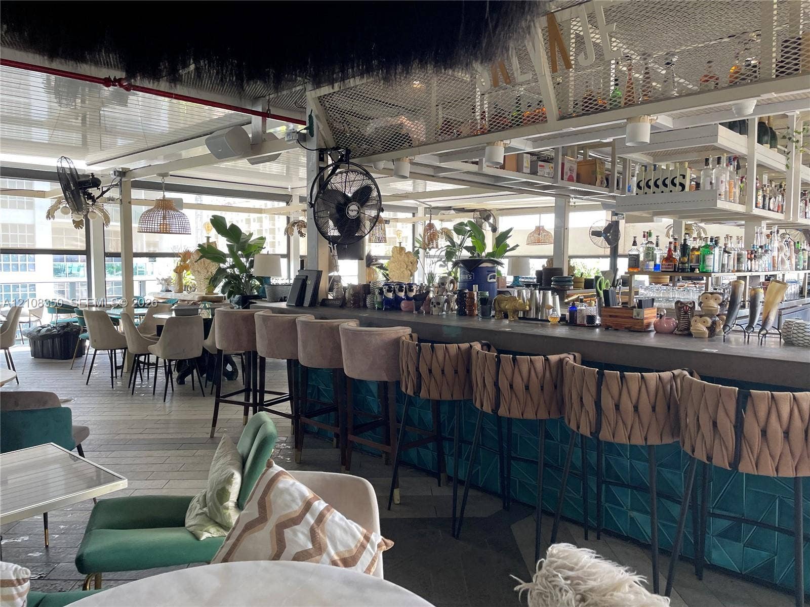 121 NE 34th Street, #1403, Miami, Miami, FL 33137 Expansive bar area featuring a solid surface countertop, geometric teal tile facade, metal mesh overhead shelving, and industrial-style wall-mounted fans