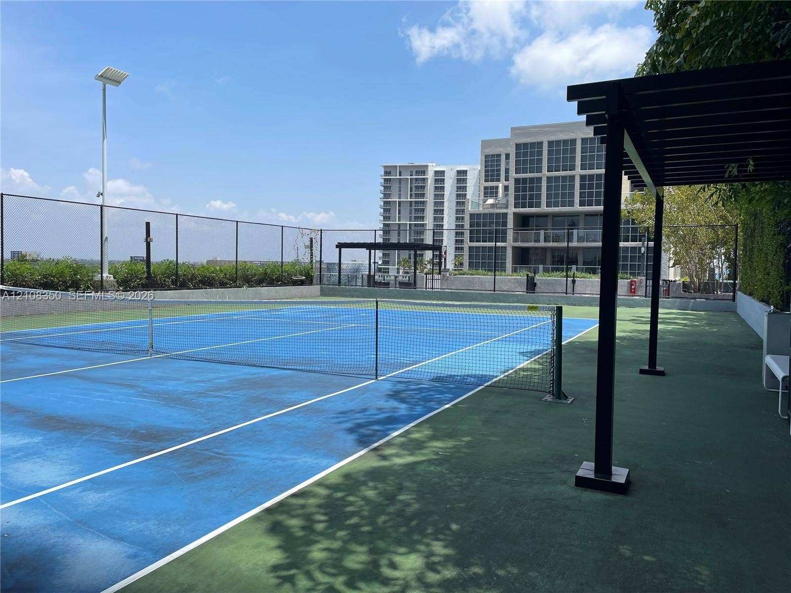121 NE 34th Street, #1403, Miami, Miami, FL 33137 Rooftop tennis court featuring a perimeter fence, overhead lighting, and a metal pergola structure
