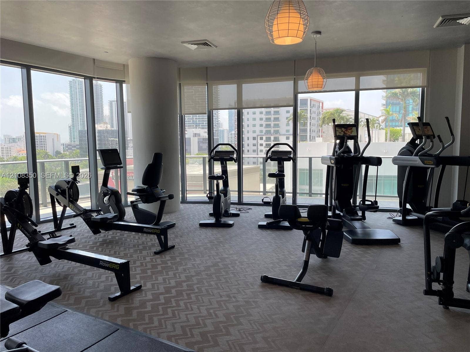 121 NE 34th Street, #1403, Miami, Miami, FL 33137 Fitness room featuring floor-to-ceiling windows, roller shades, patterned carpeting, and spherical pendant lighting