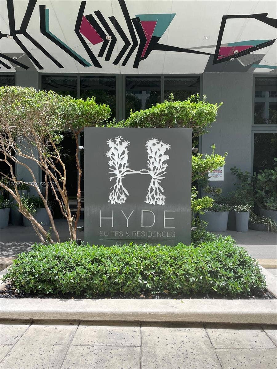 121 NE 34th Street, #1403, Miami, Miami, FL 33137 Property entrance featuring custom signage, concrete masonry, manicured shrubbery, mature landscaping, and structural ceiling art