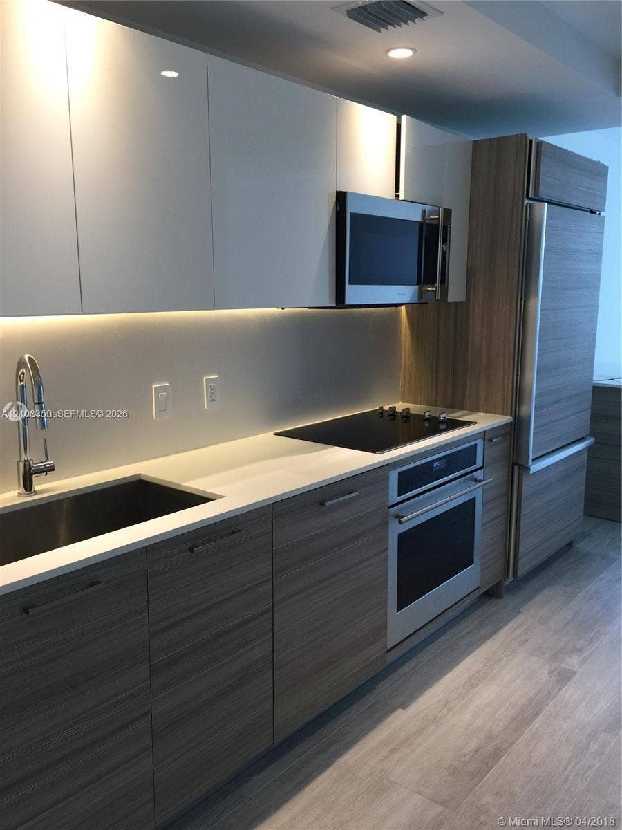 121 NE 34th Street, #1403, Miami, Miami, FL 33137 Kitchen featuring wood-finish lower cabinetry, white gloss upper cabinetry, stone countertops, stainless steel appliances, and integrated under-cabinet lighting