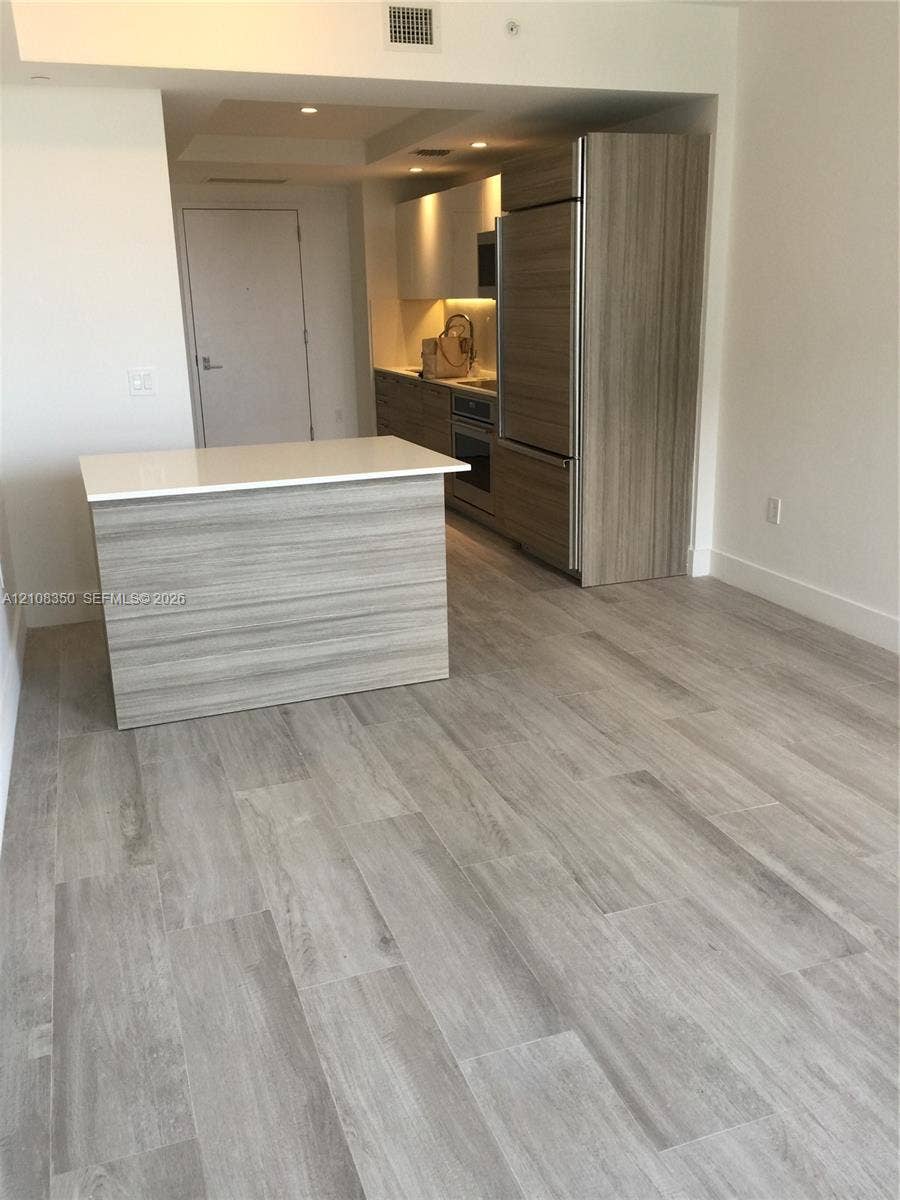 121 NE 34th Street, #1403, Miami, Miami, FL 33137 Kitchen featuring wood-finish cabinetry, a portable island with a solid-surface countertop, stainless steel appliances, and wood-finish flooring