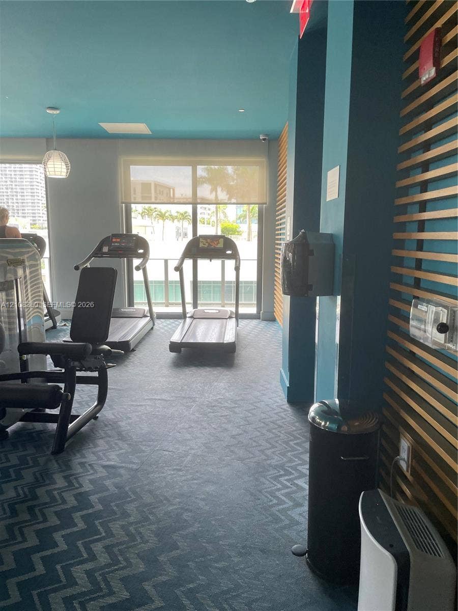 121 NE 34th Street, #1403, Miami, Miami, FL 33137 Fitness center featuring chevron-patterned carpeting, decorative wood-slat wall paneling, and floor-to-ceiling glass sliding doors with solar shades
