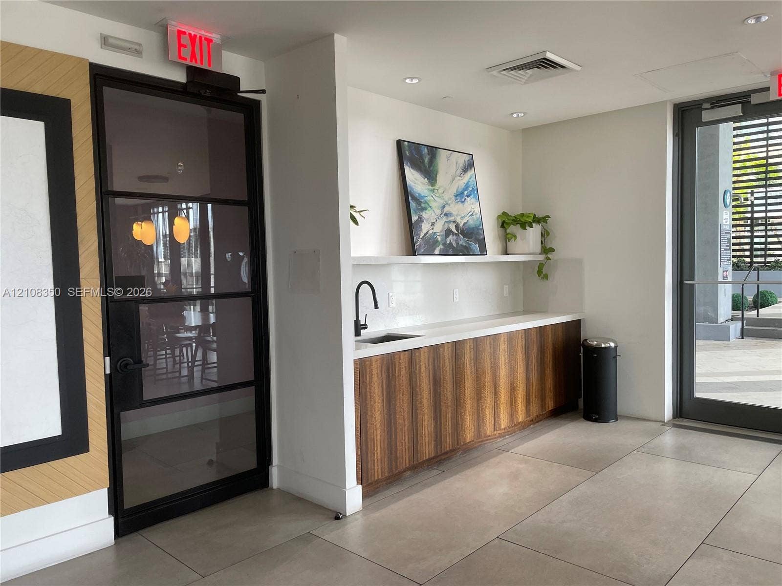 121 NE 34th Street, #1403, Miami, Miami, FL 33137 Built-in kitchenette featuring wood-veneer cabinetry, quartz countertop, and a matte black faucet, complemented by large-format tile flooring and an industrial-style metal-framed glass door