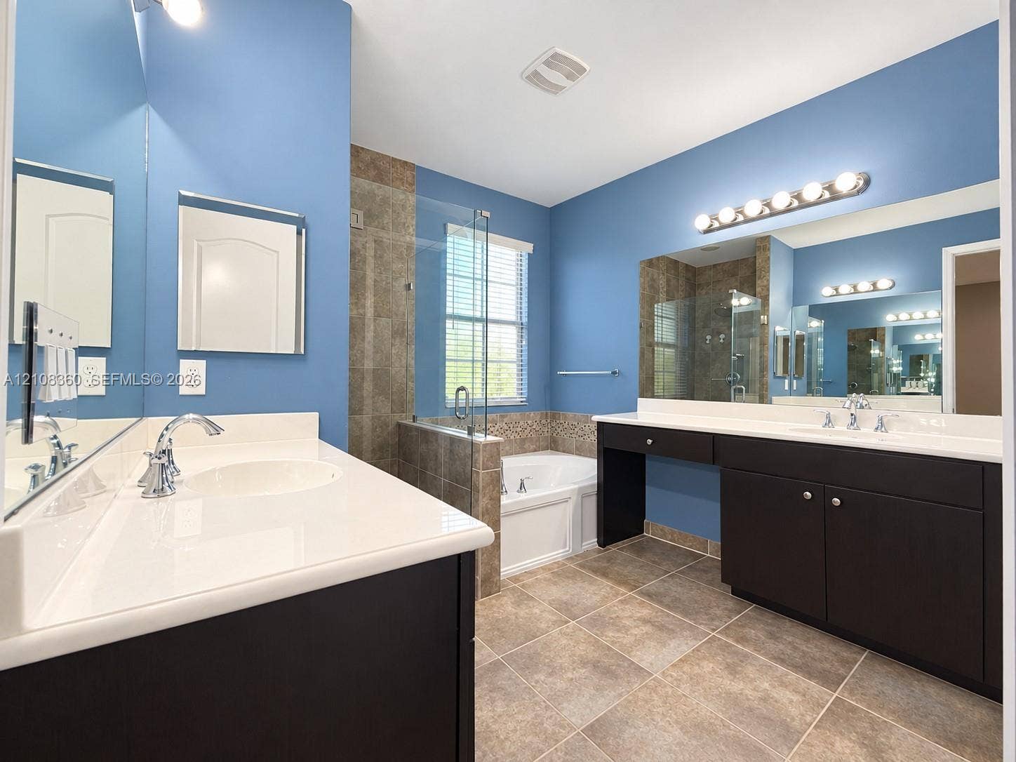 4608 Tara Cove Way, #4608, West Palm Beach, West Palm Beach, FL 33417 Bathroom featuring a dual-sink vanity with dark cabinetry, solid-surface countertops, large wall-mounted mirrors, a tiled walk-in shower with glass enclosure, and a soaking tub