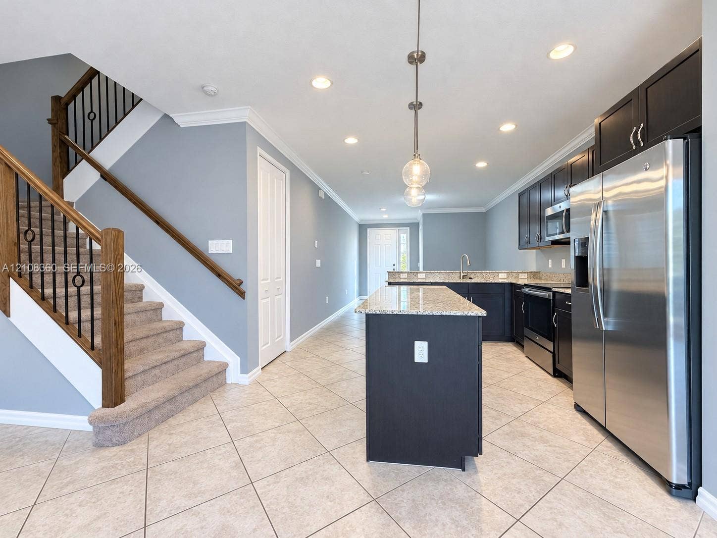 4608 Tara Cove Way, #4608, West Palm Beach, West Palm Beach, FL 33417 Kitchen featuring dark cabinetry, stone-finish countertops, stainless steel appliances, and a center island, complemented by a staircase with wooden handrails and iron balusters