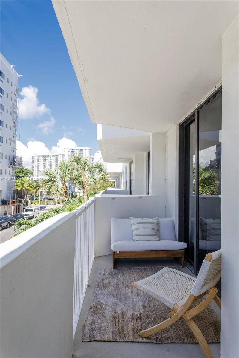 Covered balcony featuring white metal railings, concrete flooring, and sliding glass door access
