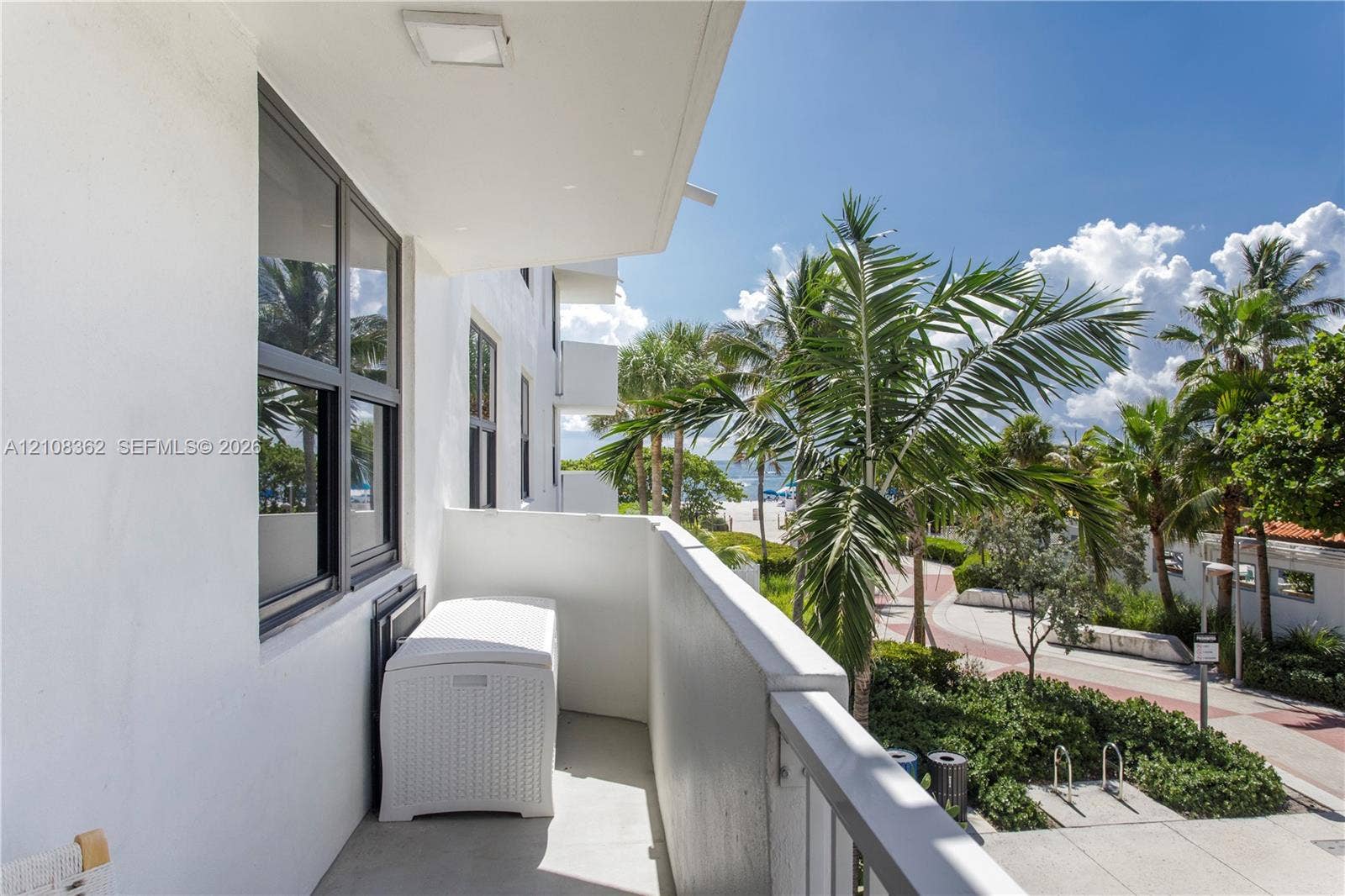 Covered balcony with smooth concrete flooring, solid masonry privacy walls, and metal railings, featuring black-framed windows