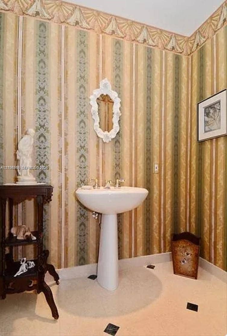 20165 NE 39 Place, #403, Aventura, FL 33180 Pedestal sink featuring metallic fixtures, decorative wallpaper with crown border detail, and tile flooring with inset accent squares