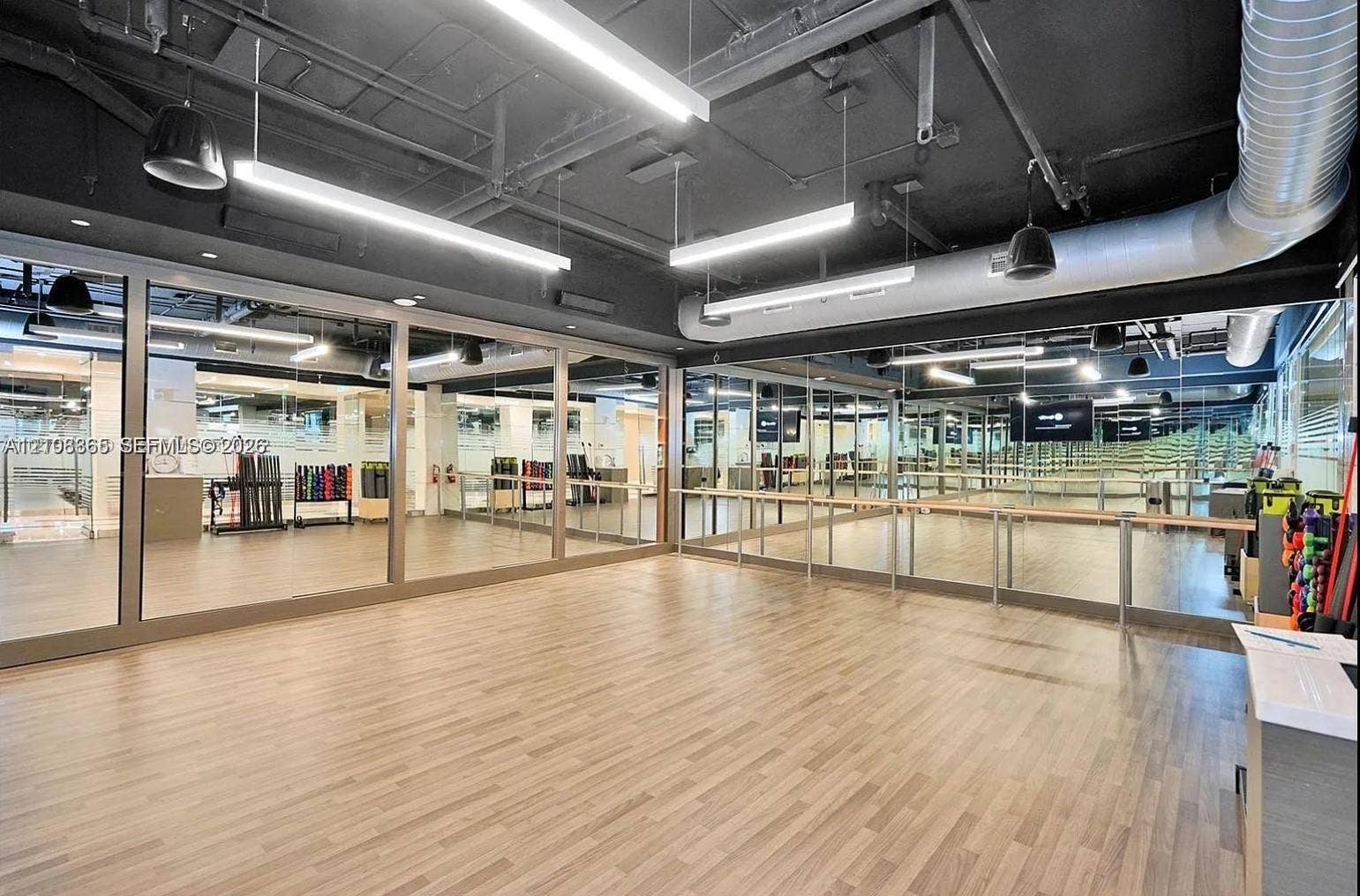 20165 NE 39 Place, #403, Aventura, FL 33180 Studio space featuring wood-finish flooring, floor-to-ceiling mirrors, exposed industrial ceiling, linear LED lighting, and a wall-mounted wooden ballet barre