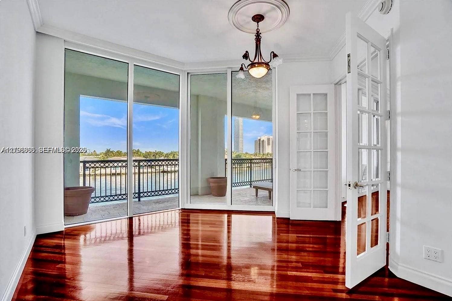 20165 NE 39 Place, #403, Aventura, FL 33180 Room featuring polished wood-finish flooring, floor-to-ceiling glass paneling, a decorative ceiling medallion with an attached chandelier, and French-style interior doors