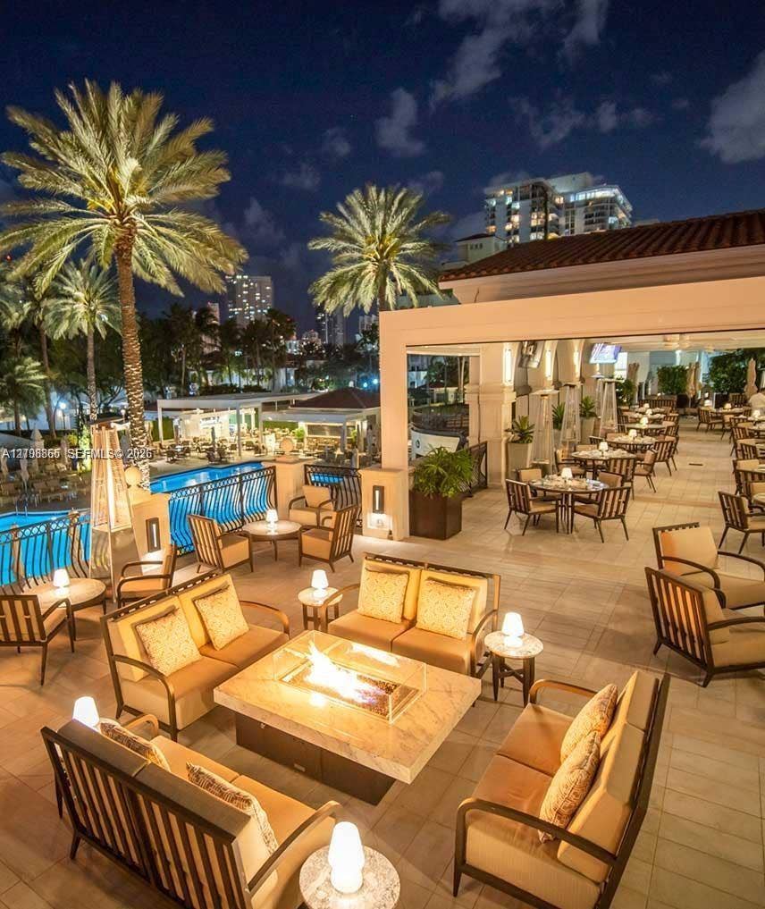20165 NE 39 Place, #403, Aventura, FL 33180 Expansive outdoor terrace featuring stone flooring, a built-in fire pit with a stone surround, and an integrated swimming pool with metal safety railing