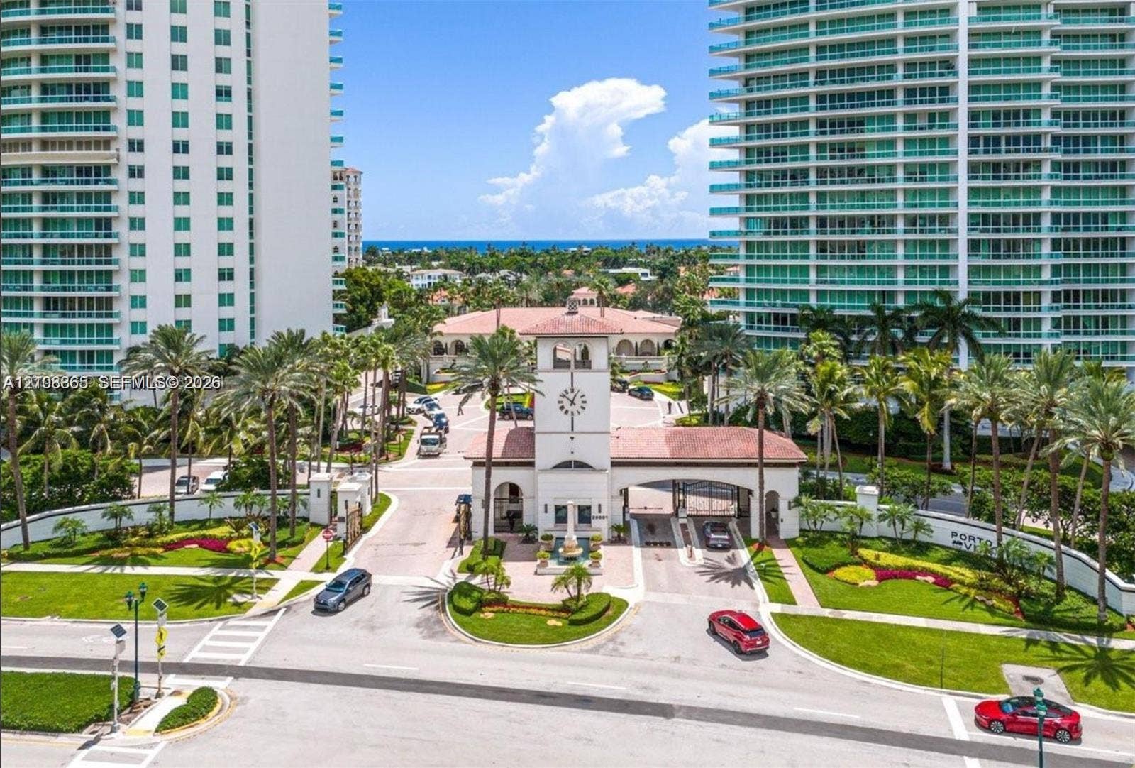 20165 NE 39 Place, #403, Aventura, FL 33180 Gated entrance featuring a clock tower, terracotta-tiled roofs, manicured landscaping, and palm-lined grounds