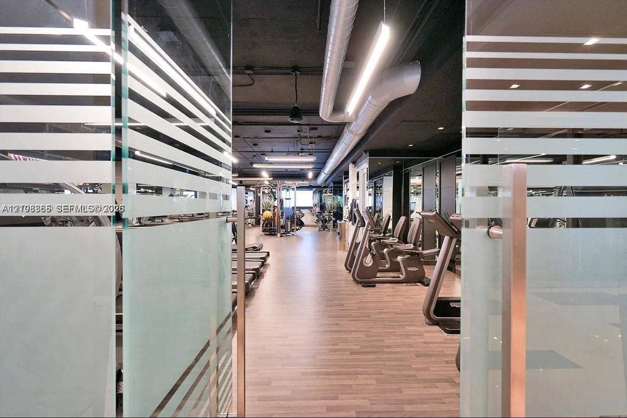 20165 NE 39 Place, #403, Aventura, FL 33180 Glass doors with frosted horizontal detailing, wood-finish flooring, exposed industrial-style ceiling with ductwork, and linear overhead lighting