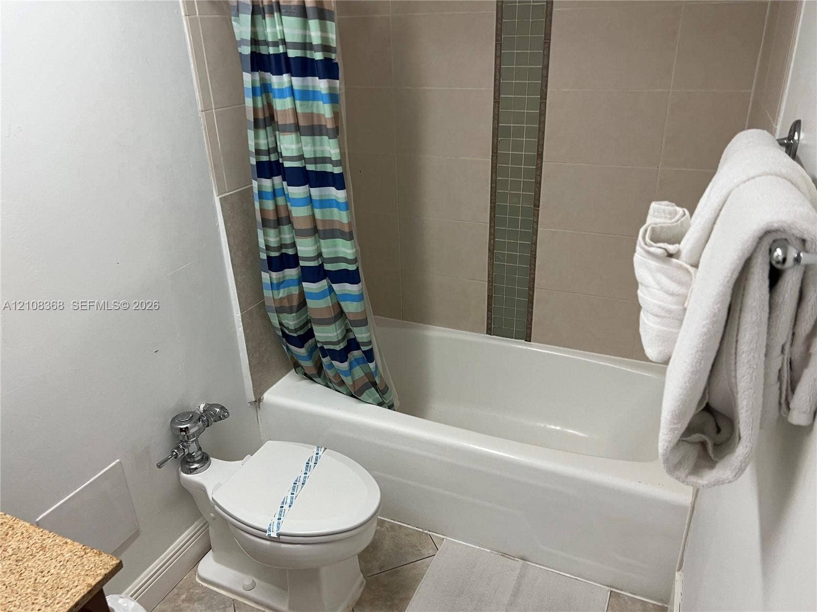 Full bathtub enclosure featuring neutral ceramic wall tile with a vertical decorative glass mosaic accent strip and tile flooring
