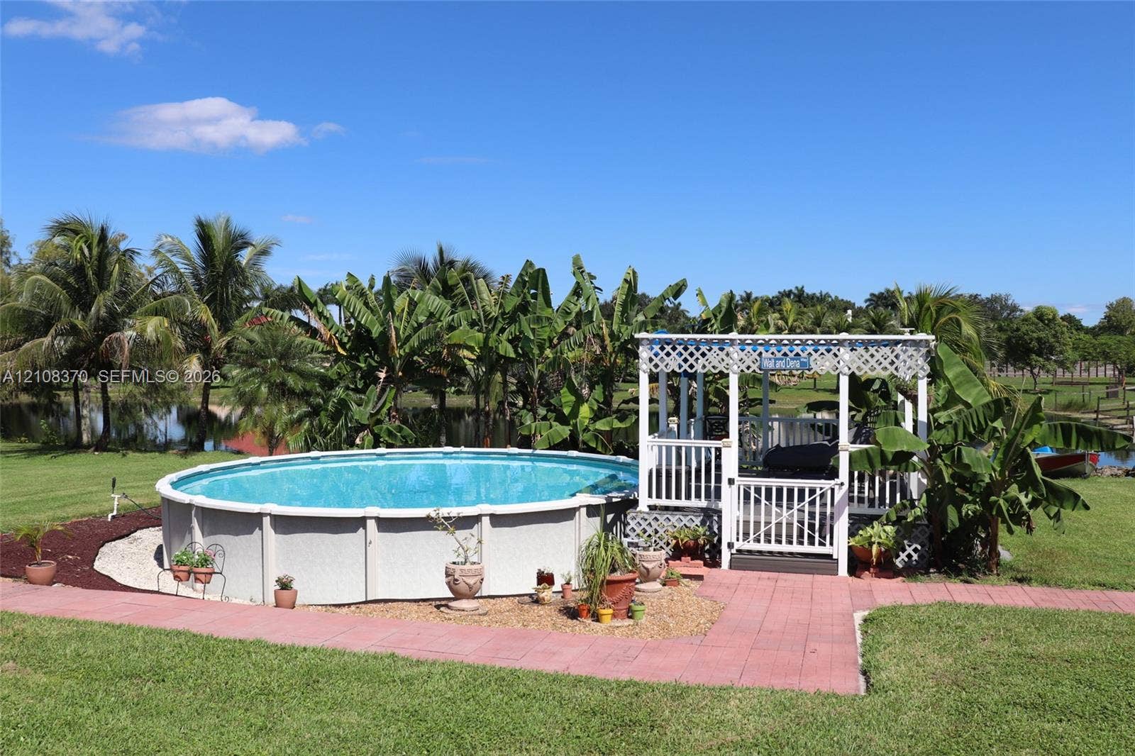 18901 SW 63rd Street, Southwest Ranches, FL 33332 Above-ground swimming pool with surrounding gravel landscaping, accompanied by a white lattice-covered gazebo featuring an integrated deck and gate
