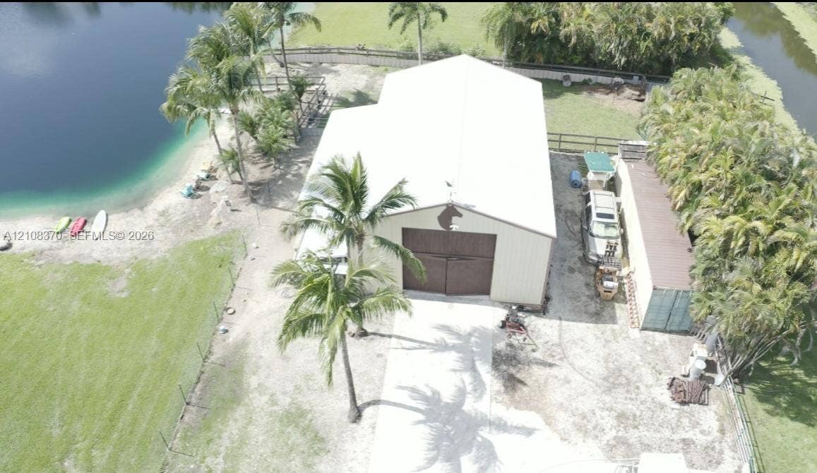 18901 SW 63rd Street, Southwest Ranches, FL 33332 Detached metal workshop featuring dual sliding doors, a white exterior finish, concrete driveway, and direct water frontage on a landscaped lot