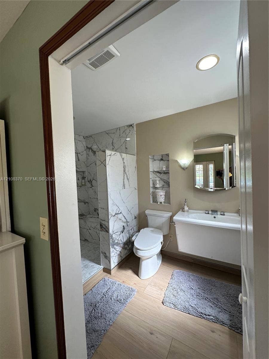 18901 SW 63rd Street, Southwest Ranches, FL 33332 Walk-in shower with floor-to-ceiling veined tile surround, recessed wall shelving, wall-mounted vanity, and wood-finish flooring