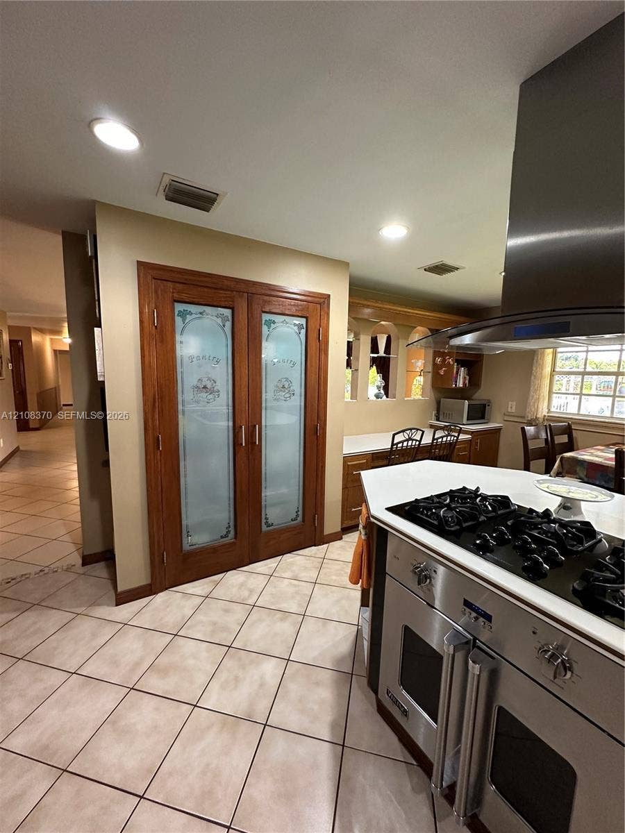 18901 SW 63rd Street, Southwest Ranches, FL 33332 Double pantry with frosted glass paneled doors, stainless steel gas range with overhead ventilation hood, recessed lighting, and tile flooring