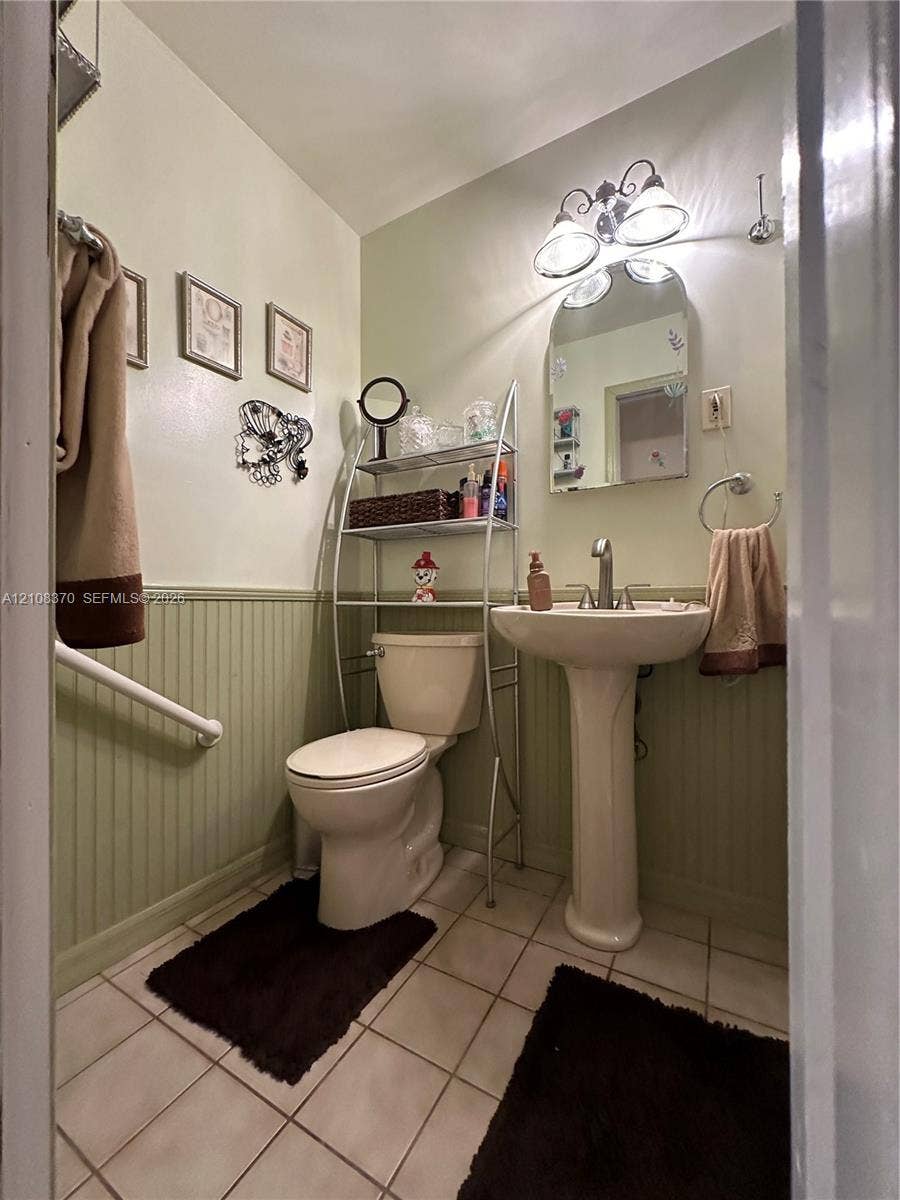 18901 SW 63rd Street, Southwest Ranches, FL 33332 Ceramic tile flooring, pedestal sink with metal faucet, beadboard wainscoting, arched wall-mounted mirror, and three-bulb vanity lighting
