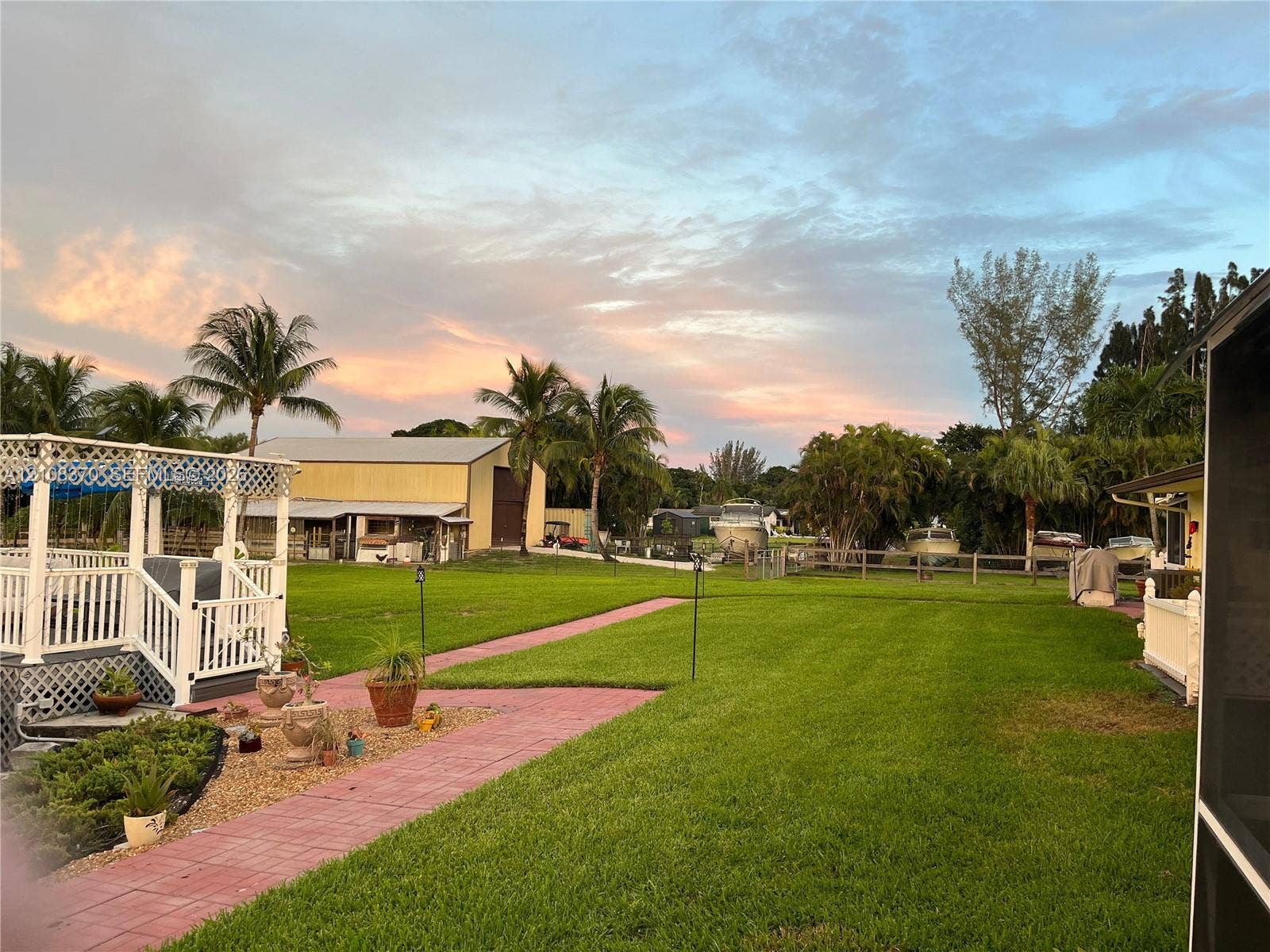 18901 SW 63rd Street, Southwest Ranches, FL 33332 Expansive backyard featuring a manicured lawn, a paved stone walkway, a multi-level white wood-finish deck, and a detached metal-sided outbuilding