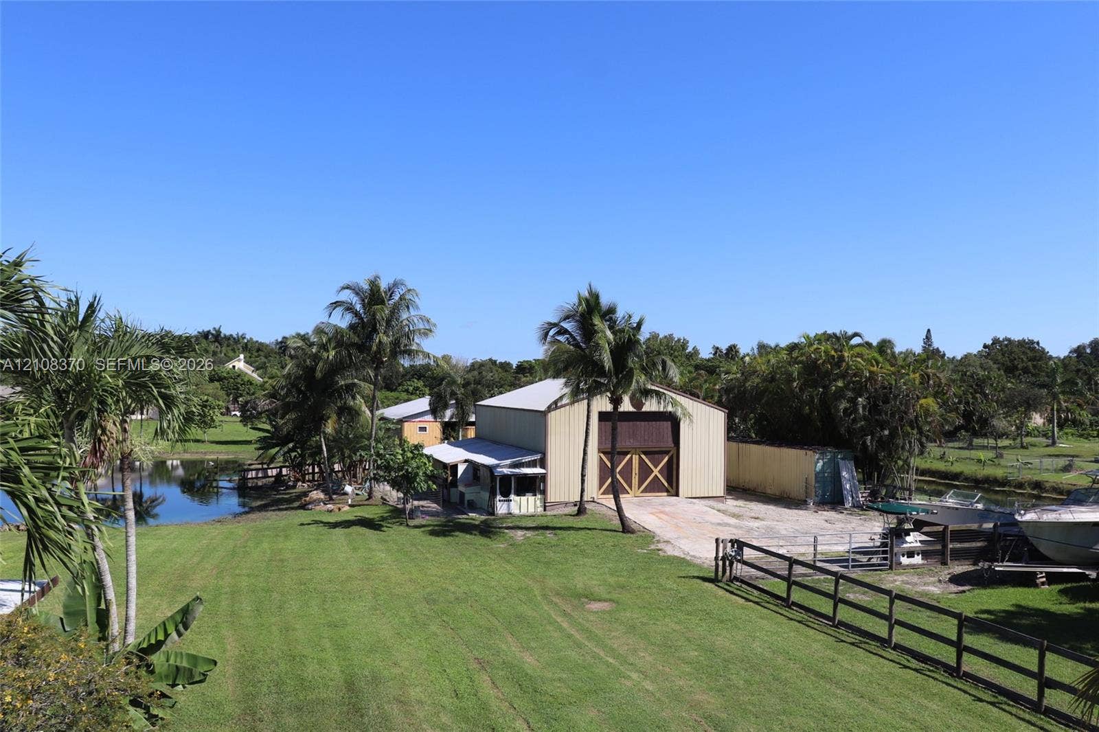18901 SW 63rd Street, Southwest Ranches, FL 33332 Expansive grounds featuring a metal-sided workshop with dual-entry doors, a grass lawn, mature palms, and bulkhead water access