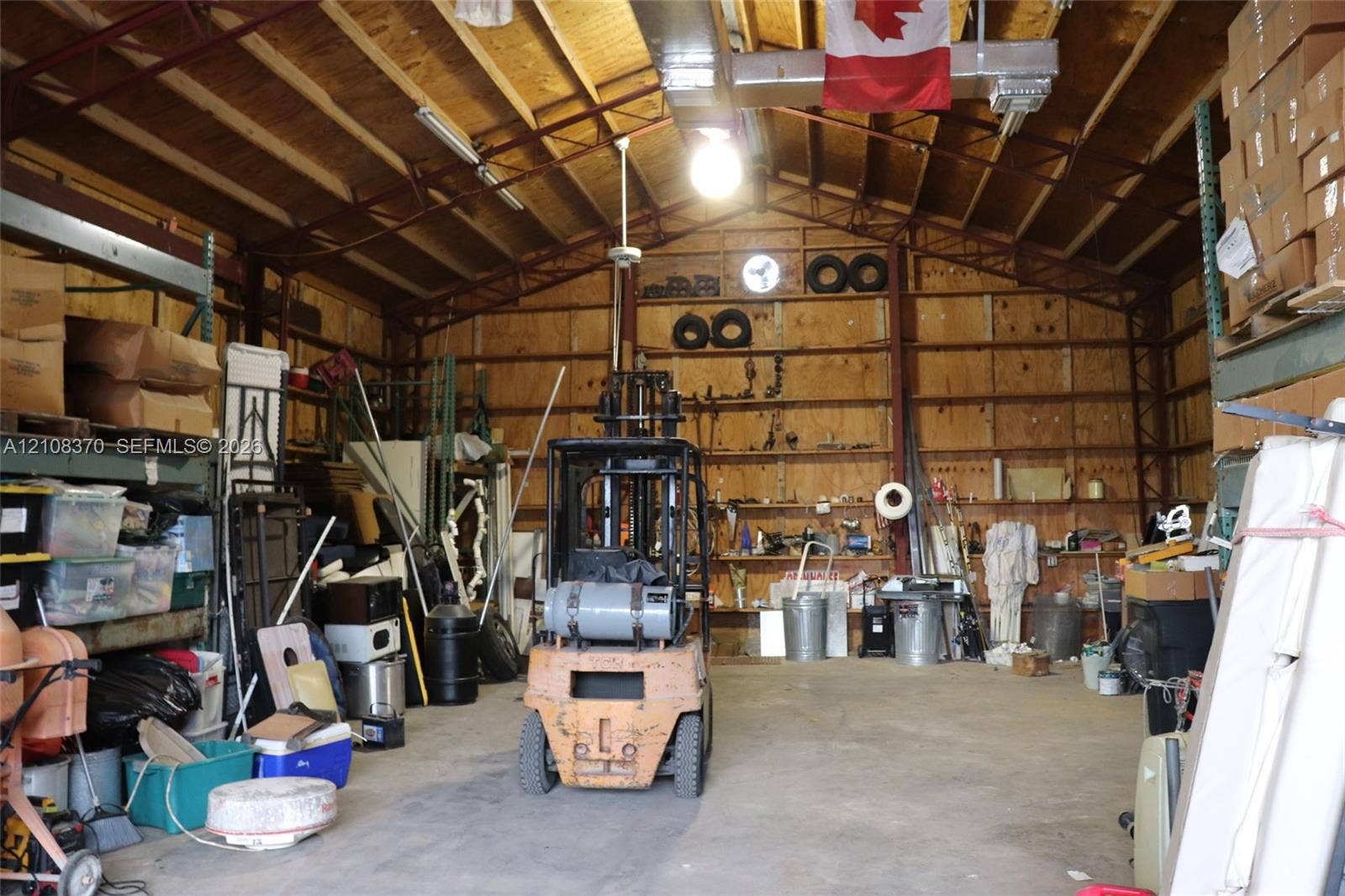 18901 SW 63rd Street, Southwest Ranches, FL 33332 Spacious industrial-style workshop featuring high vaulted ceilings, exposed structural metal framing, reinforced concrete flooring, and extensive wall-mounted open shelving