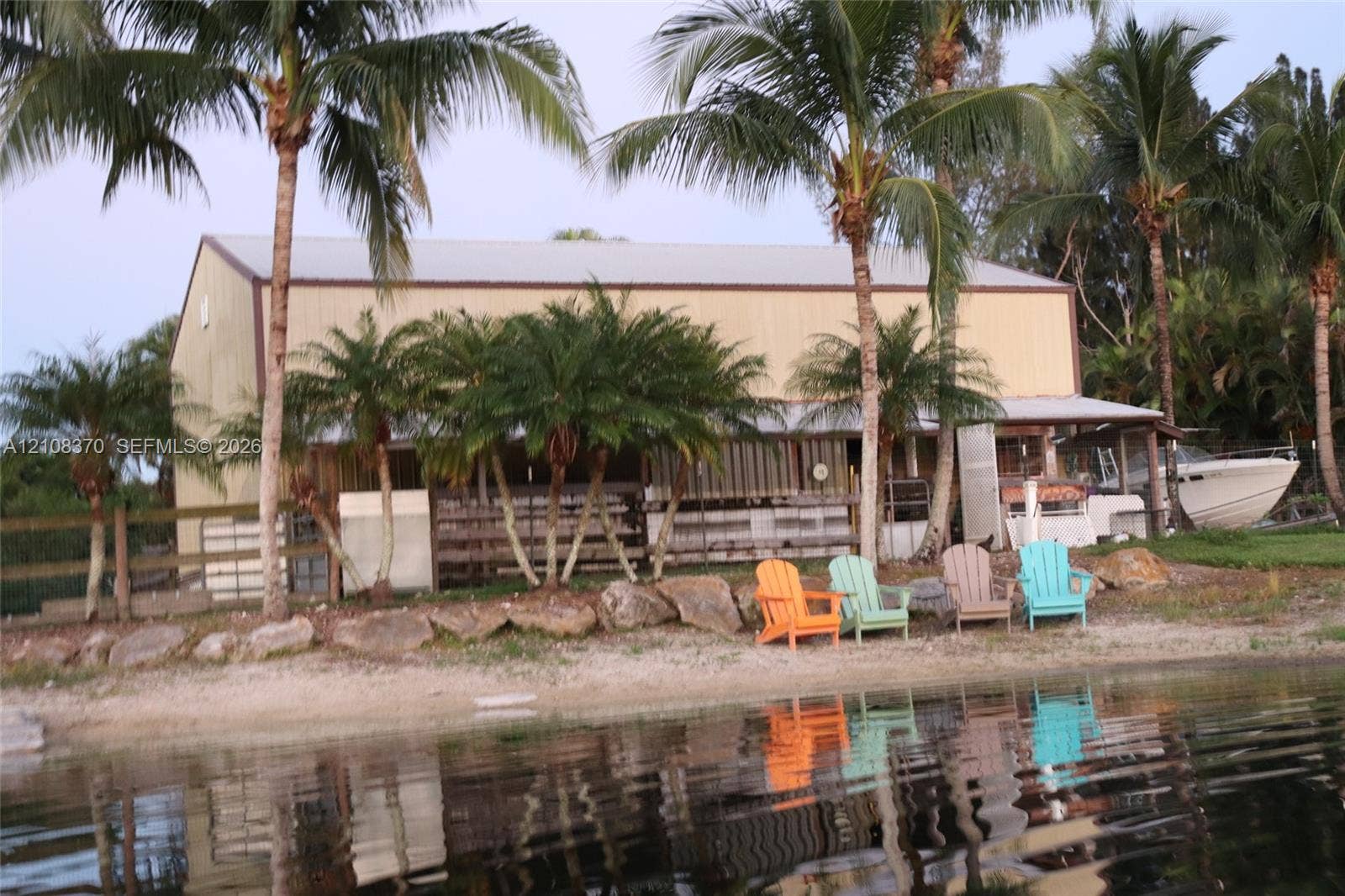 18901 SW 63rd Street, Southwest Ranches, FL 33332 Waterfront structure featuring a metal roof, stacked stone riprap, and perimeter fencing surrounded by mature palm trees