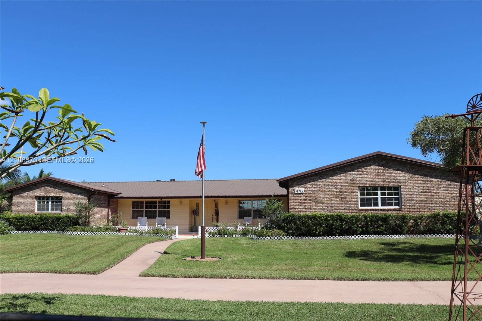 18901 SW 63rd Street, Southwest Ranches, FL 33332 Single-story brick exterior featuring a metal roof, front covered porch, manicured lawn, and ornamental windmill structure
