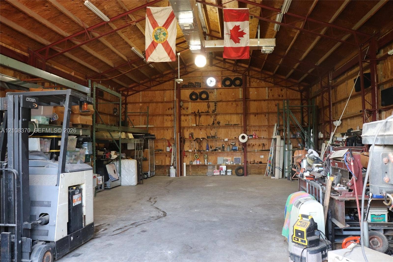 18901 SW 63rd Street, Southwest Ranches, FL 33332 Expansive metal-framed workshop featuring exposed truss construction, high ceilings, concrete flooring, plywood wall paneling, and integrated fluorescent lighting