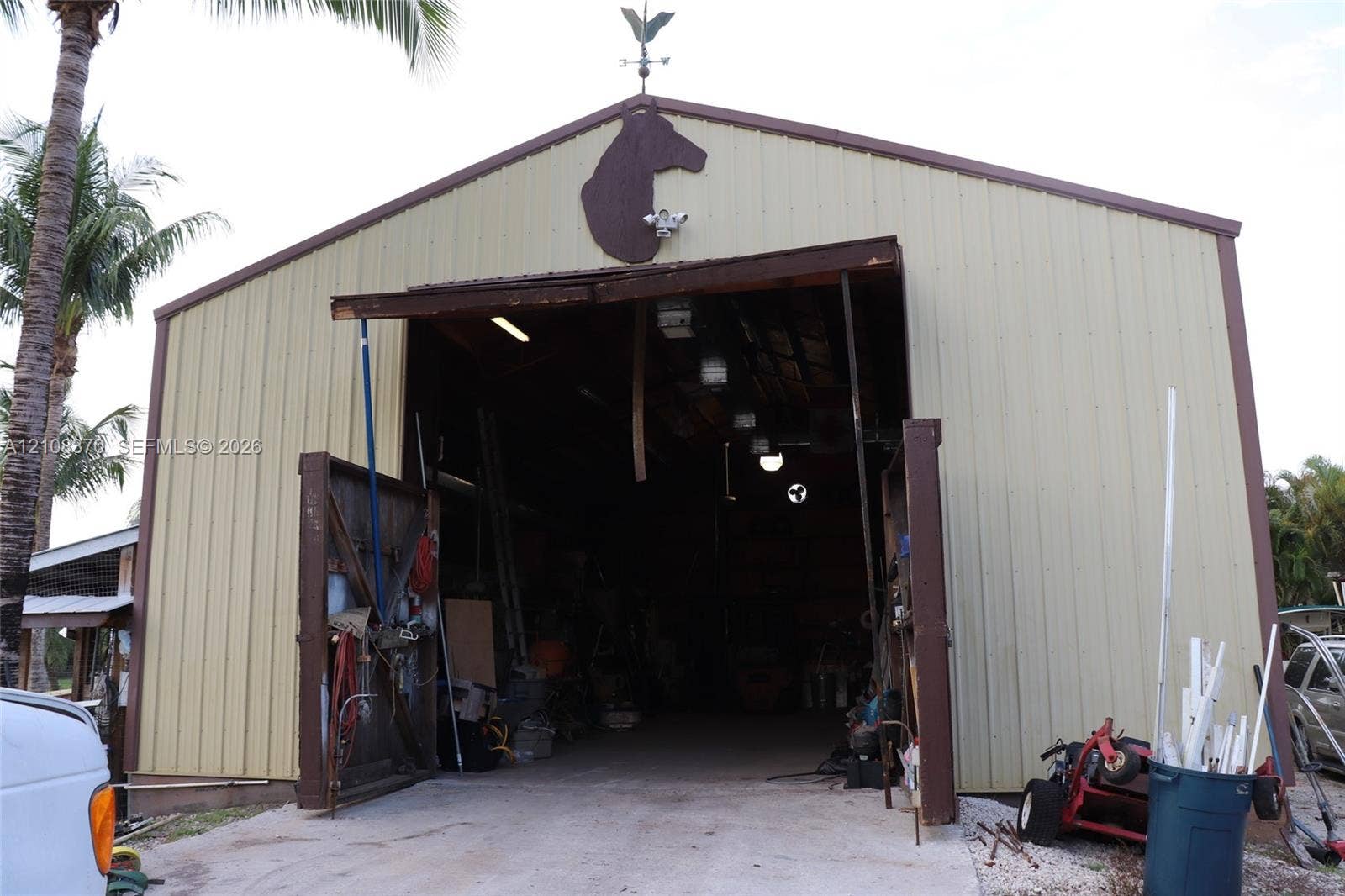 18901 SW 63rd Street, Southwest Ranches, FL 33332 Metal-sided outbuilding featuring a high-clearance entrance, swinging door mechanisms, and a decorative roof-mounted weather vane